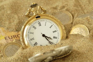 pocket watch with money half buried in sand